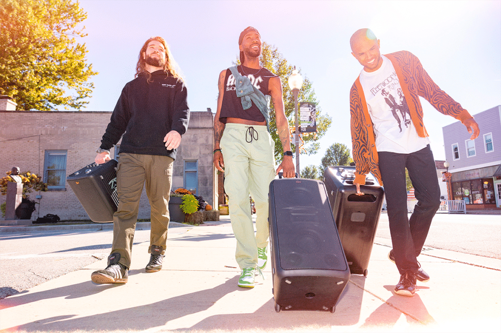 Kolme henkilöä kuljettaa Klipsch bilekaiuttimia pyörillä ulkona