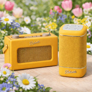 Keltainen Roberts Uno BT -radio ja Roberts Beacon 325 -kaiutin keväisessä kukka-asetelmassa puupinnalla.